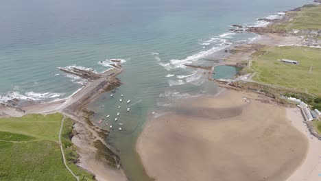 Aerial-orbital-of-Summerleaze-Beach-in-Bude,-Cornwall,-featuring-the-wide-stretch-of-sand,-coastal-vegetation,-and-the-nearby-ocean-waves