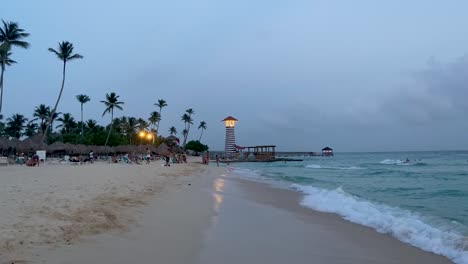 Beach-at-dusk-with-lighthouse-in-Bayahíbe-Dominican-Republic,-people-relaxing-by-the-shore