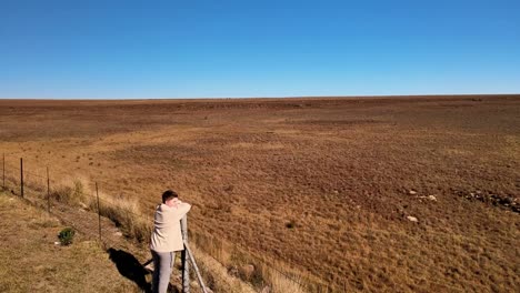 Caucasian-boy-resting-on-a-fence-post,-gazing-into-the-vast,-open-grasslands-in-complete-freedom