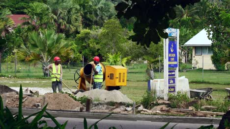 Indische-Bauarbeiter-Unterhalten-Sich-Bei-Der-Arbeit,-Während-Sie-Putzstaub-In-Den-Mischer-Werfen,-Um-Den-Fußgängerweg-In-Der-Nähe-Der-Straße-Zu-Bauen