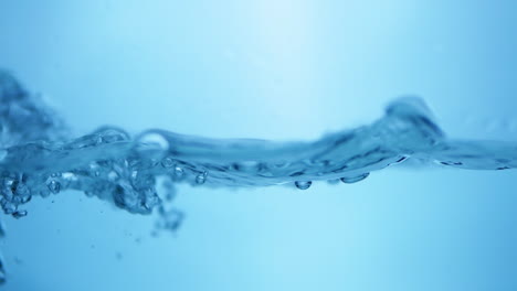 Pouring-into-a-half-filled-container-creating-waves,-ripples-and-droplets-of-water-against-a-blue-background