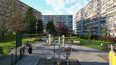 Outdoor-gym-during-a-beautiful-summer-day-surrounded-by-lush-greenery,-grass-and-trees-under-a-clear-blue-sky---drone-view-4K