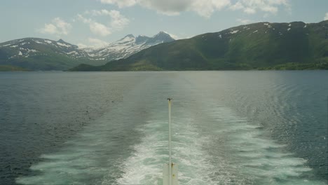 Ferry-crossing-Arctic-Circle-with-snowy-mountains-in-the-background-and-calm-sea-water-during-summer