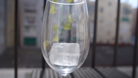 Hermosa-Toma-En-Cámara-Lenta-Que-Muestra-Cómo-Se-Colocan-Un-Par-De-Cubitos-De-Hielo-Dentro-De-Un-Vaso-De-Vidrio-En-Una-Terraza-A-La-Luz-Del-Sol.