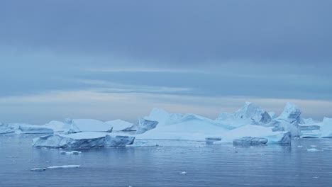 Antarctica-Iceberg-Scenery-at-Sunset,-Large-Massive-Blue-Icebergs-with-Amazing-Shapes-and-Dramatic-Couds-and-Sky-in-Sunrise-Winter-Seascape-Landscape-on-Antarctic-Peninsula