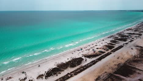 Das-Bild-Ist-Eine-Luftaufnahme-Eines-Strandes-Mit-Kristallklarem-Wasser-In-Mahdia,-Wo-Die-Menschen-Verschiedene-Aktivitäten-Genießen