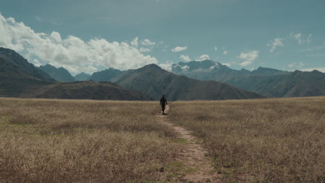 Man-walking-from-behind-towards-mountains-raises-hands-in-sign-of-triumph