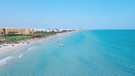 La-Imagen-Es-Una-Vista-Aérea-De-Una-Playa-Con-Agua-Azul-Cristalina-De-Un-Hotel-En-Mahdia,-Donde-La-Gente-Disfruta-De-Diversas-Actividades.