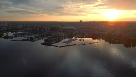 Imágenes-Aéreas-Tomadas-Con-Un-Dron-Que-Capturan-Una-Vibrante-Puesta-De-Sol-Sobre-Un-Puerto-Deportivo-De-La-Ciudad-Con-Barcos-Y-Edificios-Frente-Al-Mar