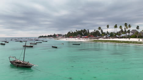 Aerial-flyover-clear-water-of-Zanzibar-Island-,-with-sandy-beach-and-parked-boats