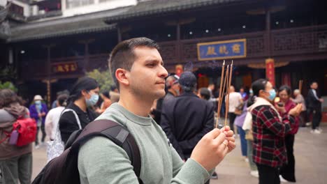 Spanish-tourist-holding-incense-sticks-at-God-City-Temple-in-Shanghai,-surrounded-by-Chinese-locals