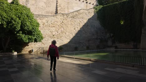 Turista-Caminando-Y-Mirando-Hacia-La-Impresionante-Muralla-Exterior-De-La-Catedral-De-Mallorca,-Disfrutando-De-La-Arquitectura-Histórica-En-Un-Día-Soleado-Y-Brillante.