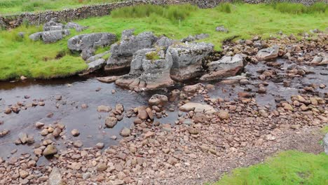 Little-Dale-Beck-River-flowing-over-rocks-and-pebbles-in-a-lush-green-landscape-below-Whernside