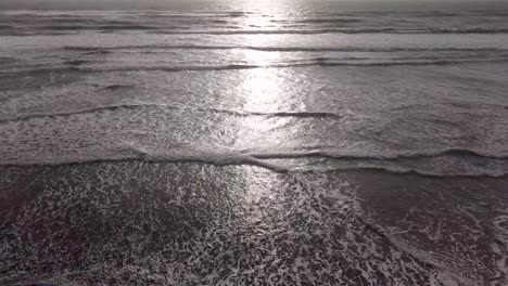 Sun-at-dusk-illuminates-waves-at-Piha-Beach,-New-Zealand,-with-a-warm-glow