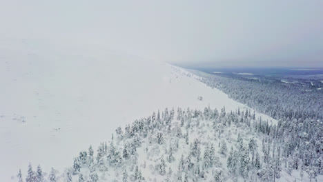 Aerial-view-flying-along-the-snowy-Luosto-fell,-cloudy-winter-day,-in-Lapland