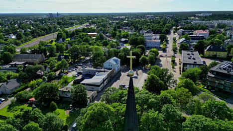 Aerial-orbit-around-roof-European-catholic-church-with-cross,-green-cityscape