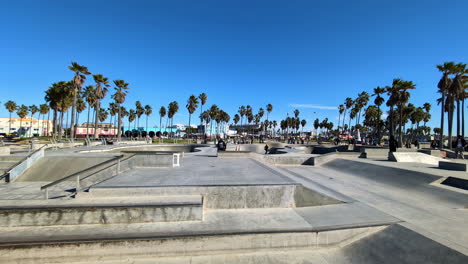 Blick-Auf-Einen-Skatepark-An-Einem-Sonnigen-Tag,-Mit-Palmen-Im-Hintergrund-Und-Skateboardern-Und-Bikern,-Die-Die-Rampen-Genießen