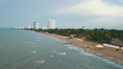 Vista-Aérea-De-La-Playa-De-Palo-Blanco-En-Sucre,-Colombia,-Que-Muestra-Las-Olas-Costeras,-Los-Hoteles-Junto-A-La-Playa-Y-La-Exuberante-Vegetación.