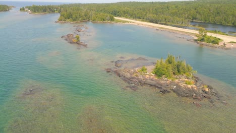 Aerial-drone-footage-of-clear-coastal-waters-with-rocky-formations-and-lush-shoreline