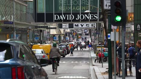 Downtown-shopping-precinct-featuring-David-Jones-and-Myer-flagship-stores-in-bustling-Melbourne-city,-with-pedestrians-crossing-and-busy-vehicle-traffic,-street-scene-of-Little-Bourke-Street