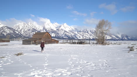 Mujer-Solitaria-Caminando-Sobre-La-Nieve-Frente-A-Un-Puesto-De-Madera,-Tierras-De-Cultivo-En-El-Campo-Estadounidense,-Cámara-Lenta