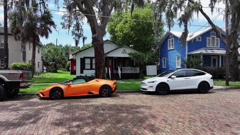 Orangefarbener-Lamborghini-Und-Weißer-Tesla-Parken-Auf-Der-Straße-In-Einem-Amerikanischen-Viertel-Mit-Palmen