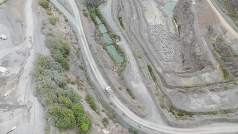 Orbital-aerial-view-of-a-large-industrial-truck-carrying-mined-aggregate-from-the-quarry-base,-highlighting-the-quarry's-scale-and-activity