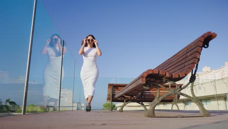 Female-tourist-in-long-white-dress-walk-glass-safety-barrier,-Mallorca