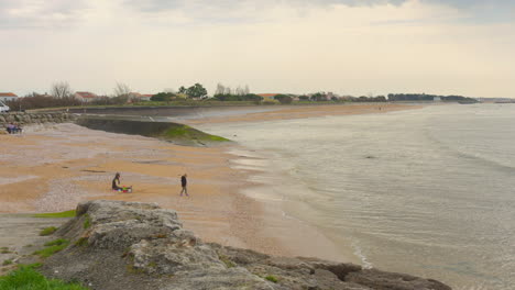 Pan-shot-of-an-empty-beach-in-La-Rochelle,-France-with-father-and-son-playing-in-sand