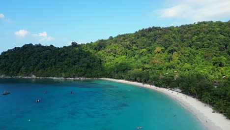 Tropischer-Strand-Mit-Türkisfarbenem-Wasser,-Weißem-Sand-Und-üppiger-Grüner-Vegetation,-Boote-Ankern-In-Der-Nähe-Der-Anlegestelle