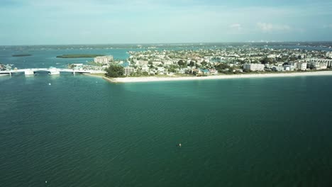 Aerial-shot-of-John's-Pass-Bridge-in-Florida,-connecting-coastal-areas-over-blue-waters,-with-buildings-and-greenery