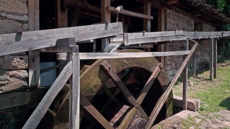 El-Agua-Que-Cae-En-Cascada-Desde-Un-Canal-De-Madera-Rústica-Hace-Girar-Una-Gran-Rueda-Hidráulica-De-Molino-De-Madera