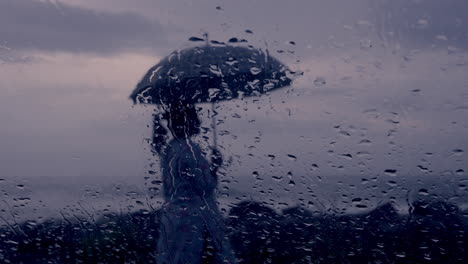 Regentropfen-Rieseln-Bei-Starkem-Regen-Auf-Das-Nasse,-Klare-Autofensterglas-Mit-Blick-Auf-Den-Strand,-Eine-Dame-Mit-Regenschirm-Genießt-Den-Regnerischen-Tag-Der-Monsunzeit