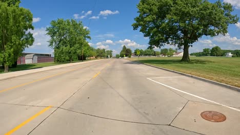 POV---Driving-on-city-street-past-fenced-in-tennis-courts-and-an-open-soccer-field-in-Moline-Illinois