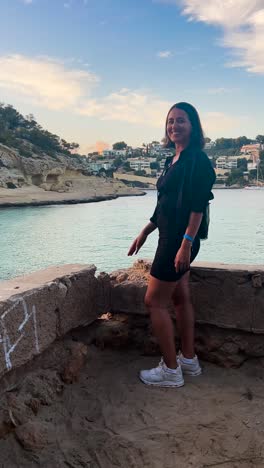 Vertical---woman-near-tropical-water-bay-point-finger-to-city-landscape,-Spain