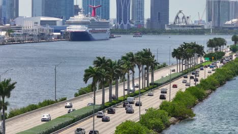 Toma-Aérea-Del-Tráfico-En-La-Calzada-De-MacArthur-Con-Una-Tienda-De-Cruceros-Y-El-Horizonte-De-Miami-Al-Fondo