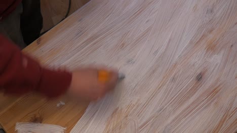 Worker-paints-wooden-table-with-white-color-with-brush-from-the-paint-bucket