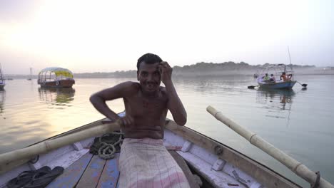 A-local-Indian-fisherman-with-bare-body-sailing-traditional-wooden-boat-in-Ganga-river-Triveni-Sangam-in-evening-with-tourists,-confluence-of-the-Ganges,-Yamuna,-and-Saraswati-River