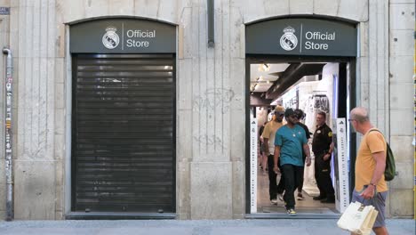 Shoppers-are-seen-leaving-the-official-brand-store-of-the-Spanish-professional-football-club-Real-Madrid,-as-pedestrians-walk-past-the-frame-in-Spain