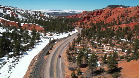 Rotes-Geländewagen-Fahrzeug,-Das-An-Einem-Sonnigen-Wintertag-Auf-Einer-Staatsstraße-In-Der-Landschaft-Von-Utah,-USA,-Unterwegs-Ist-Und-Drohnenaufnahmen-Verfolgt