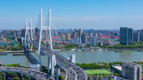 Bird's-view-of-multi-level-junction-road-lands-moving-cars-traffic-of-modern-highway-with-overpass-bridge-at-countryside-with-boat-flow-in-lake-near-high-skyscrapers-skyline-high-building-real-estate