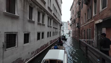 Gondolas-gliding-through-a-canal-between-historic-buildings-in-Venice,-Italy