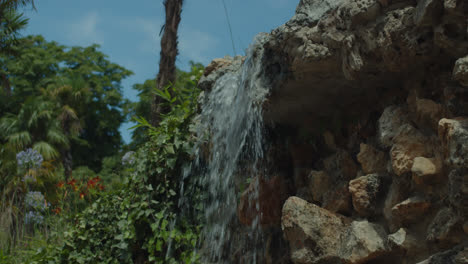 Beautiful-slow-motion-shot-of-a-waterfall-in-a-pond-with-rocks-inside-“El-Retiro-Park”-in-Madrid,-Spain-in-daylight