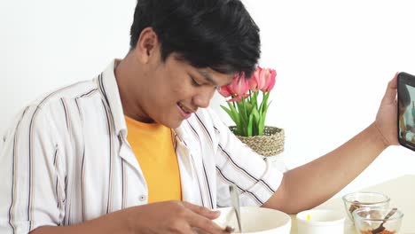 Un-Joven-Asiático-Disfruta-Comiendo-Y-Mostrando-Fideos-A-La-Cámara-Mientras-Graba-Un-Video-Con-Un-Teléfono-Móvil