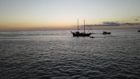 Drone-shot-flying-over-the-ocean-surface-with-a-large-wooden-ship-ahead,-then-flying-over-the-ship's-masts