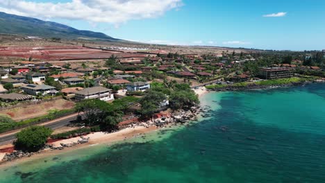 Drone-orbits-rocky-outcropping-on-tropical-beach-with-road-and-mountain-view