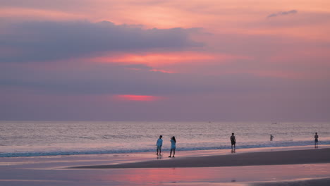 Silhouetted-Group-of-Tourists-Watching-Spectacular-Dramatic-Sunset-at-Seminyak-Beach-Seashore-in-Bali---wide-angle,-slow-motion,-copy-space