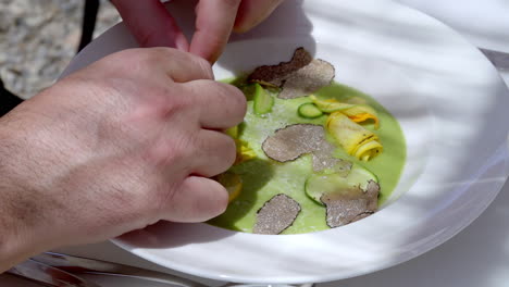 close-up-of-a-chef's-hands-delicately-plating-a-gourmet-dish-with-truffle-slices,-zucchini,-and-squash-blossoms-in-a-green-sauce