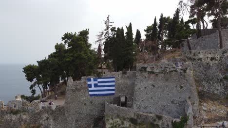 Castillo-Veneciano-De-Parga,-Murallas-Con-Bandera-Griega-Y-Algunos-Turistas-De-Visita