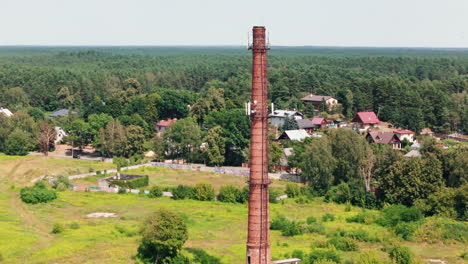 Torre-De-Telefonía-Móvil-Construida-Sobre-Una-Antigua-Chimenea-En-Un-Campo-Con-Casas-Al-Fondo.